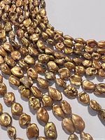 Close-up photo showing individual gold Keshi pearls on a string, displaying their unique irregular shapes and golden luster.