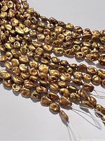 Close-up view of several strands of irregularly shaped golden Keshi pearls, showing their size and shape detail.