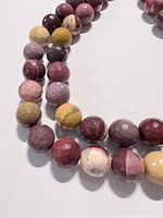 Close-up image showing round, faceted beads with natural multicolor tones including red, yellow, purple, cream, and brown hues.