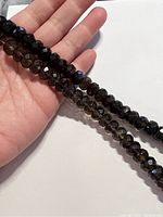 Two strands of faceted roundel smoky quartz beads held in hand showing color and size.