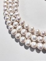 Close-up of three strands of large freshwater pearls 10-11mm size, showing surface texture and luster well.