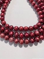 Photo showing three strands of burgundy freshwater pearls laid out on a white background, highlighting their shape and color.