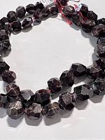 Close-up of dark red garnet nugget beads on strand, showing bead shapes and faceting.