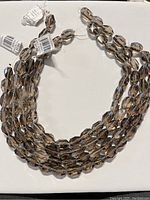 Four strands of faceted smoky quartz beads arranged on a white background with tags visible on some strands.