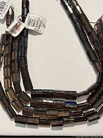 Four strands of smoky quartz beads arranged with visible tags, showing natural translucent dark brown color and flat cylinder shapes.