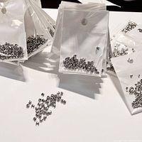 Plastic bags containing numerous small white gold plated crimp covers spread out on a white surface.