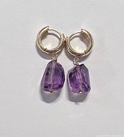Close-up image of the earrings laid flat on a white background showing the gold hoop and raw cut amethyst stones.