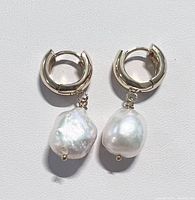 Pair of gold plated hoop earrings with irregular shaped freshwater baroque pearls dangling from each hoop shown on a white background.