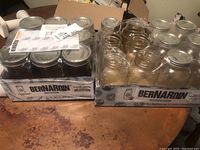 Two rectangular boxes each holding sets of Bernardin mason jars. One box sealed with 9 jars of 750 ml capacity appearing brand new with metal lids and sealing bands. The other box unsealed containing 12 jars of 1 liter each without lids visible.
