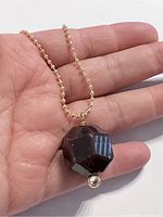 Close-up of chunky faceted garnet pendant held in palm, showing pendant details and gold plated chain