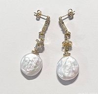 Pair of dangling earrings with coin-shaped freshwater pearls and gold plated settings with cubic zirconia on a white background.