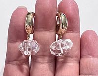 Close-up of earrings held between fingers showing natural quartz stones and gold plated hoops