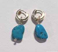 Close-up photo of two natural turquoise earrings hanging on a white background showing the 18K gold plated hoops and the irregular turquoise stones with natural veining.