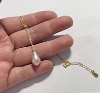 Close-up of the pink teardrop pearl pendant held in a hand showing size and detail of the pearl and gold chain.