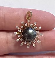 Close-up held photo showing the faceted black Tahitian South Sea pearl pendant with cubic zirconia and gold-tone 925 sterling silver setting.