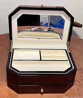 Open jewelry box with lid raised showing interior mirror and divided compartments lined in light fabric.