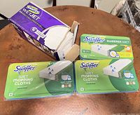 Swiffer WetJet packaging and packs of Swiffer Wet Mopping Cloths and Sweeper Wet sheets on a round wooden table