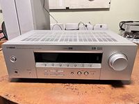 Front view of silver Yamaha AV receiver showing power button, input buttons, volume knob, and display panel.