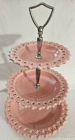 Full front view of the three-tier pink ceramic stand showing decorative cut-out edges and metal handle