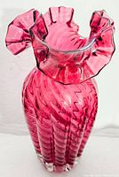 Top angled view showcasing the ruffled and crimped rim of the cranberry glass vase, highlighting its translucent deep pink color and folds.