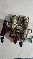 Photo showing all five vintage fishing reels assorted in a group, various colors and styles, visible manual cranks.