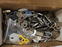 Photo of the box showing a variety of metal vintage keys, key rings, and small padlocks with some keys in plastic bag.