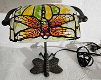 Desk lamp with power cord visible, decorative dragonfly painted on shade, metal butterfly base.
