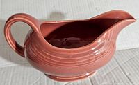 Side view of reddish-coral vintage Fiesta gravy boat showing ribbed ceramic design and handle details.