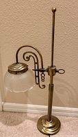 Full view of vintage brass Art Nouveau desk lamp showing tall vertical ribbed column, weighted base, decorative adjustable arm, and frosted scalloped glass shade with etched floral design.