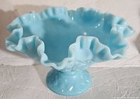 Front view of the blue glass compote showing the wide ruffled edge and pedestal base on a white surface.
