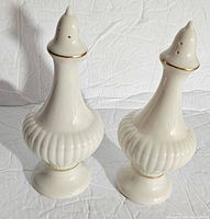 Pair of white porcelain Lenox salt and pepper shakers with ribbed sides and gold trim on a white background