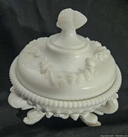 Side view showing the dish on three shell-shaped feet and the lid with detailed seashell handle and raised shell motifs.