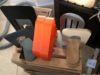 Photo showing two orange plastic Ikea bookends and several metal bookends with varying designs and colors on a wooden pallet.