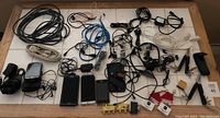 Top-down view of cables, old cell phones, HP PDA, headphones and multi-tools spread out on a white surface.
