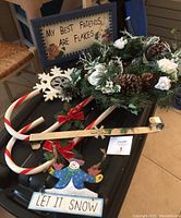Overview of the lot showing door wreath with pinecones, two large metal candy canes with red ribbons, metal snowman 'Let It Snow' wall sign, and wooden 'My Best Friends Are Flakes' sign partially visible in background