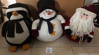 Front view of penguin, snowman, and Santa Claus stuffed Christmas decorations on tile floor