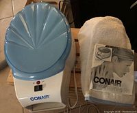Photo of the white and blue Conair Paraffin Wax Spa unit with its scalloped lid, white terry mitts, and printed manual lying next to the unit.
