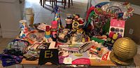 Full lot displayed on floor showing assortment of party supplies including hats, napkins, balloons, signs, ribbons, and more inside a large green metal bin.