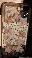 Clear iPhone 8 Plus phone case with pink and white dried flowers embedded and gold flakes scattered inside