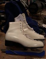 Pair of white ladies size 8 ice skates showing exterior side profile, with visible scuffs, black heel, and metal blades on blue blade guards