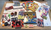 Overview of all items included in the lot on a table, showing board games, books, craft items, stickers, and small toys.