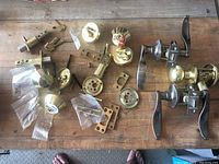 Overview of all door hardware pieces laid out on wooden floor: three door handle assemblies, miscellaneous deadbolt components including latch mechanisms, faceplates, strike plates, and screws.