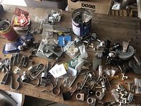 Overview of lot showing variety of metal casters, clamps, hinges, brackets and fasteners laid out on wooden table.