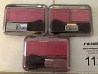 Top view showing three Clarion powder blush compacts with blush colors and applicator brushes visible inside clear lids.