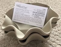 Stacked beige stoneware tortilla shell bakers with attached label showing product name and instructions.