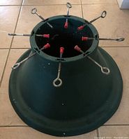 Top view of dark green plastic Christmas tree stand showing nine metal tightening screws with red plastic grips around the circular opening designed to hold the tree trunk securely
