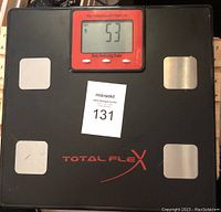 Top view of black digital body analyzing scale with red display, silver sensor pads, and Total Flex branding.