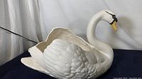Side view of large white ceramic swan with detailed feathers and curved neck, showing glaze finish and spidering.
