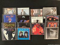 Overview of all 16 CD albums laid out on a flat surface showing a variety of bands and album covers including Billy Joel, Grateful Dead, Journey, Foreigner, Hall and Oates, The Doors, Doobie Brothers, Bruce Springsteen, Billy Ocean, Dire Straits, Jethro Tull, The Cars.