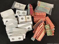 Photo showing an assortment of vintage coin wrappers in red and white stripes, coin holders with a center hole, and bundles of wrappers tied with bands.